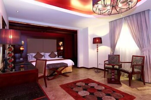 A hotel room with a bed, two chairs, a desk, a lamp, and a decorative ceiling light.
