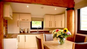 A kitchen with wooden cabinets, a sink, and a dining table with chairs. - The Cabin at Ffos Farm (Cefn cribwr)