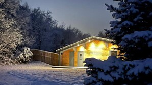A wooden cabin with a porch, surrounded by snow-covered trees. - The Cabin at Ffos Farm (Cefn cribwr)