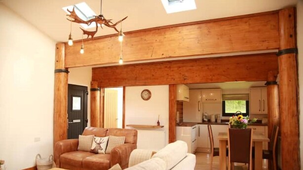 A spacious living area with a wooden ceiling, a sofa, a coffee table, and a dining table with chairs. - The Cabin at Ffos Farm (Cefn cribwr)