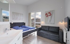Et moderne soveværelse med seng, en grå sofa, et fjernsyn og et stort vindue.
