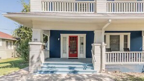 A two-story house with a red door, white railings, and a number 511 on the porch. - Private Deck & Patio with Parking- 3blks to Pearl food & fun! (San Antonio)
