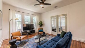 A living room with a blue sofa, a coffee table, a TV, and a ceiling fan. - Private Deck & Patio with Parking- 3blks to Pearl food & fun! (San Antonio)