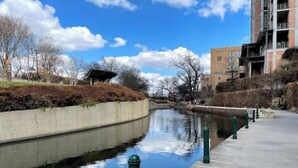 A calm water canal with a concrete walkway on one side and a building on the other. - Private Deck & Patio with Parking- 3blks to Pearl food & fun! (San Antonio)