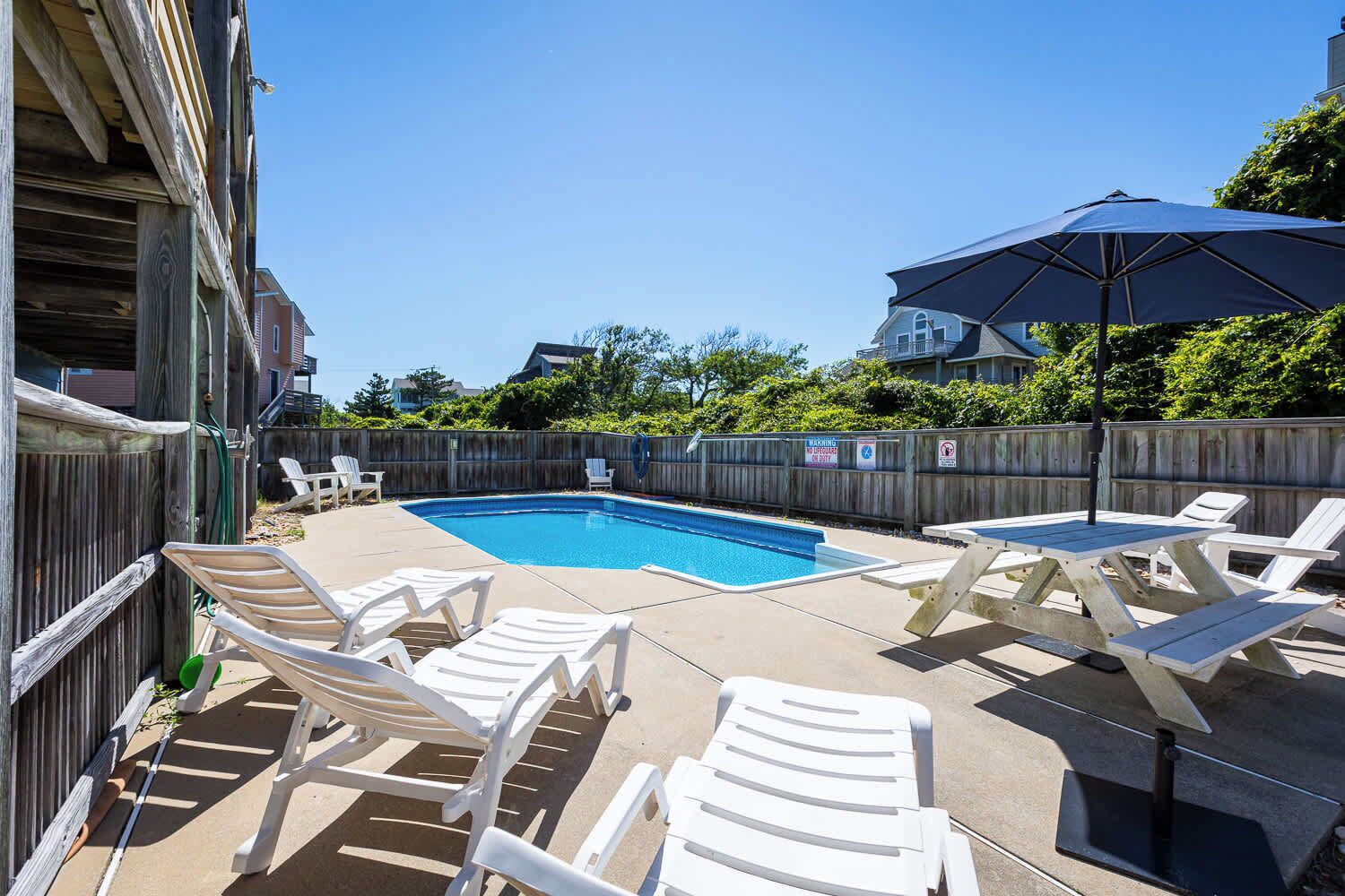 A backyard with a swimming pool, white lounge chairs, and a wooden fence.