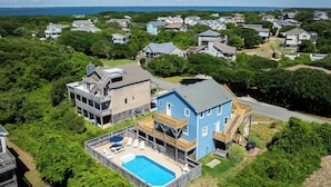 Uma casa grande com piscina, cercada por árvores e outras residências.