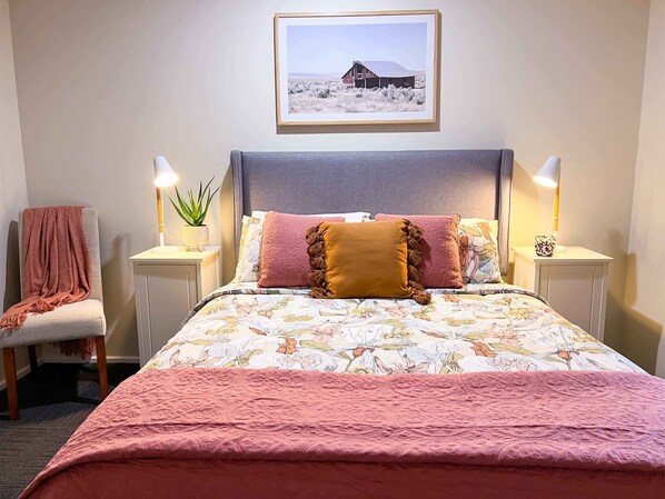 A neatly arranged bedroom with a bed, two bedside tables, a chair, and a framed picture on the wall. - Spring cottage • Family 4BR Retreat •Walk to Nowra (Nowra)