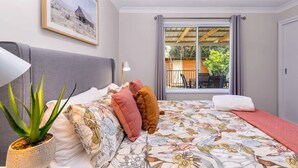 A bedroom with a bed, pillows, a potted plant, a window with curtains, and a ceiling fan.