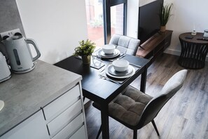A modern kitchen with a dining area, featuring a kitchen island, a dining table set for two, and a comfortable seating arrangement. - Birtin Works Apartments - Brand New - City Centre (Sheffield)