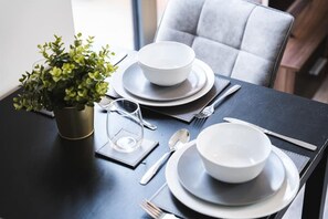 Mesa de jantar posta com tigelas, pratos, talheres e um vaso de planta.