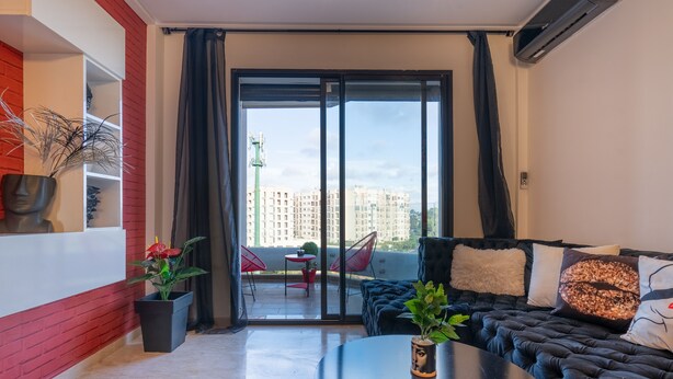 A modern living room with a black sofa, a round coffee table, and a balcony with red chairs. - Maryline's waterfall with Piscine & Rooftop (Casablanca)