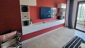 A modern living room with a red brick wall, a mounted TV, built-in shelves, and a large window. - Maryline's waterfall with Piscine & Rooftop (Casablanca)