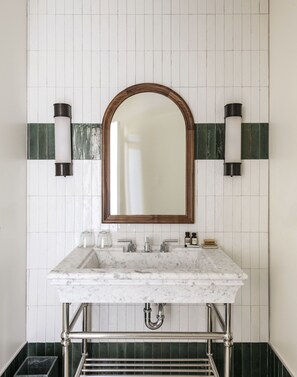 A bathroom with a marble sink, a large mirror, and two wall-mounted lights. - The Quoin Hotel (Wilmington)