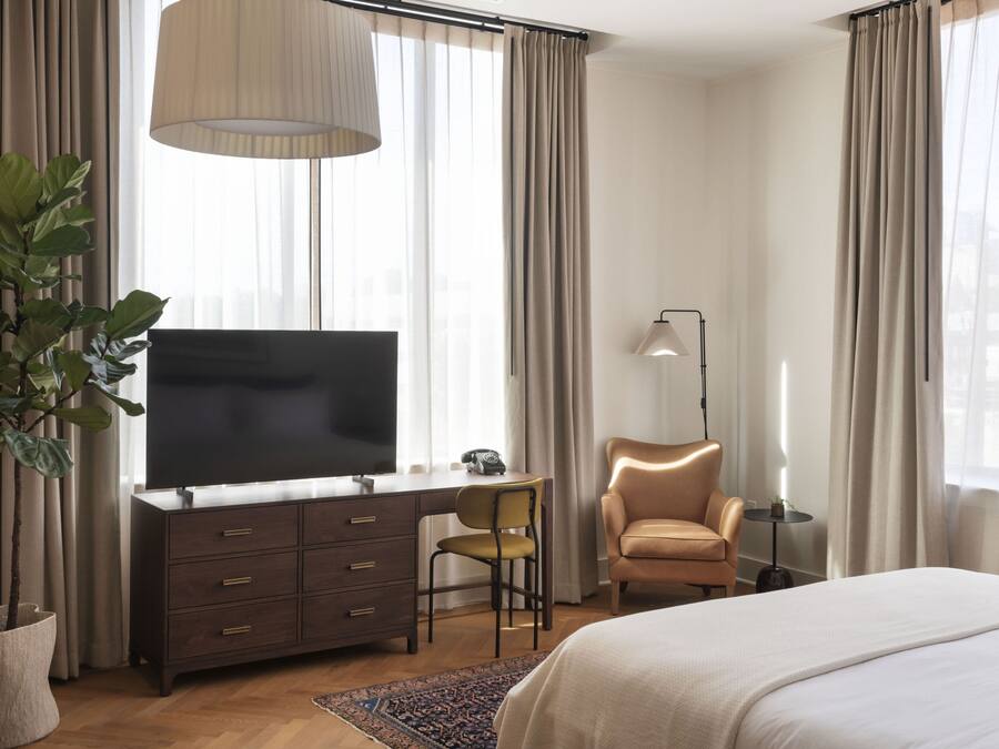 Ein Hotelzimmer mit großem Flachbildfernseher, Schreibtisch mit Stuhl, Sofa und Bett.