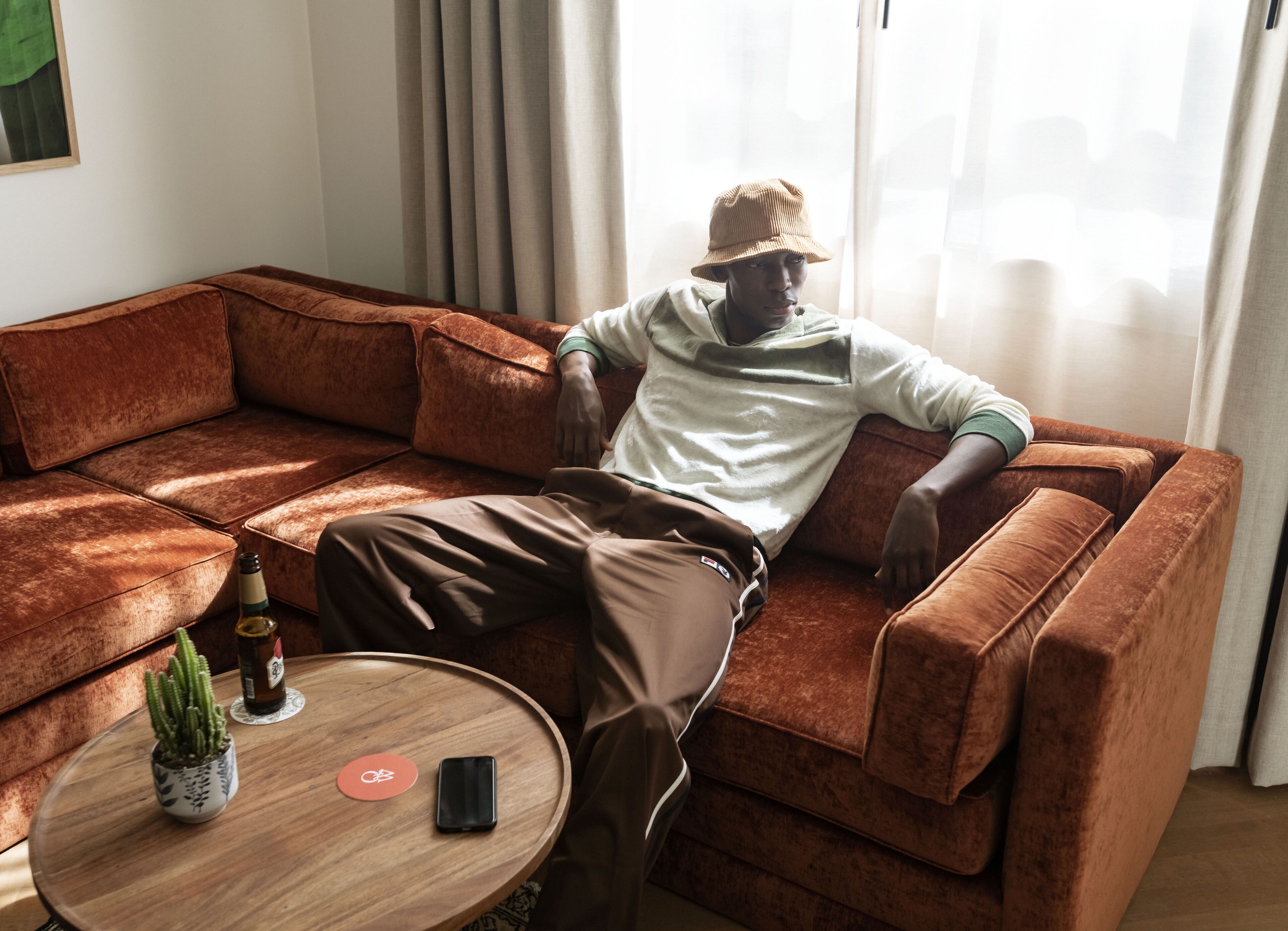 A person sitting on a brown sectional sofa in a room with a wooden coffee table, a small potted plant, and a smartphone.