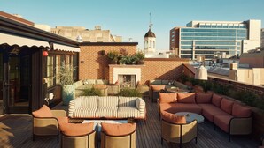 A rooftop terrace with outdoor seating, a fireplace, and a view of the city skyline. - The Quoin Hotel (Wilmington)