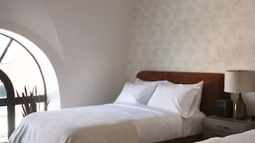 Habitación de hotel con una cama grande, una cama más pequeña, una mesita de noche con una lámpara y un papel tapiz estampado.
