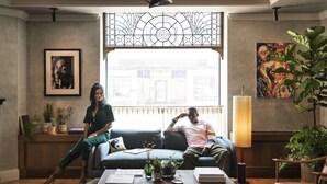 A modern living room with a large window, a sofa, a coffee table with books, and a lamp. - The Quoin Hotel (Wilmington)