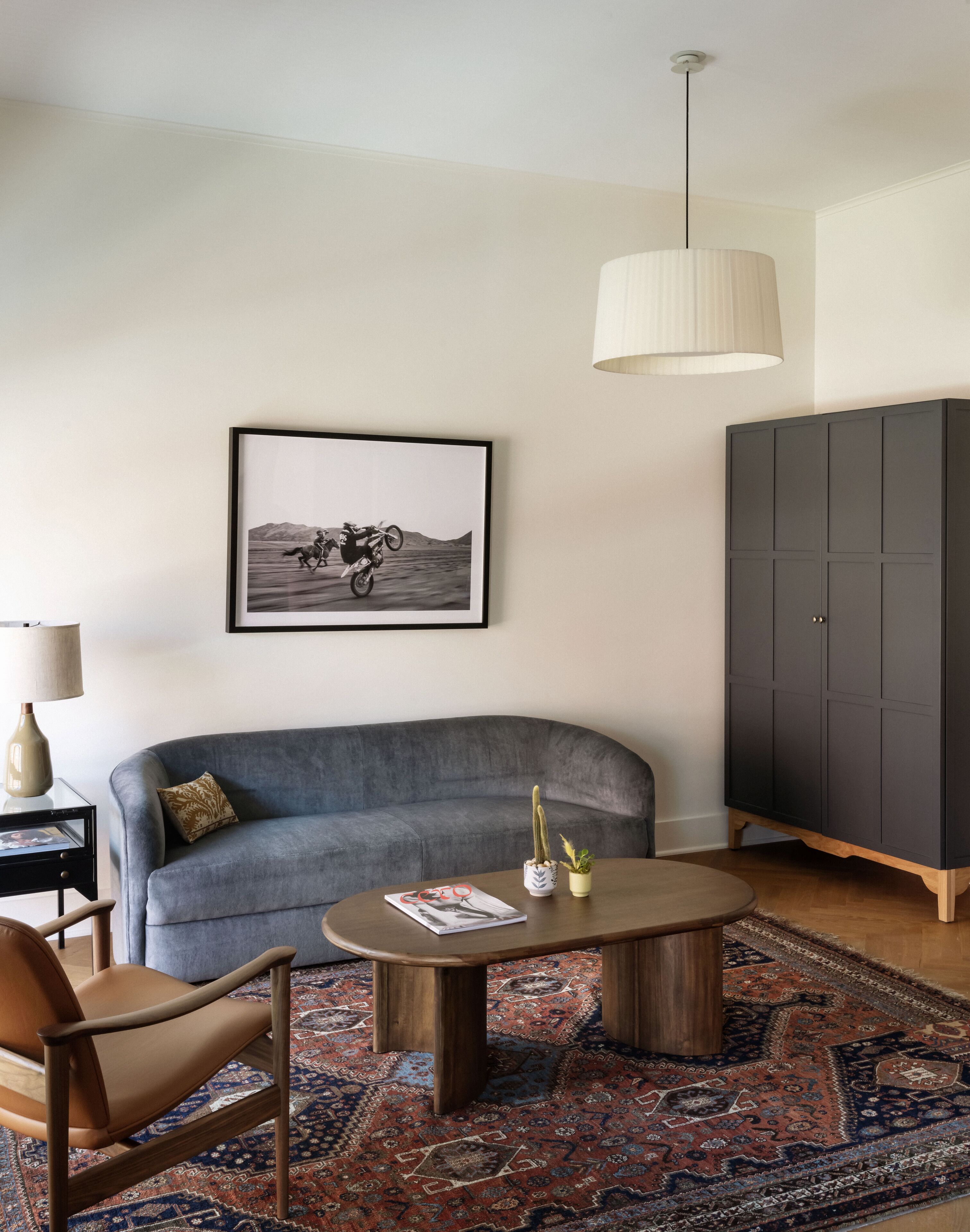 Un soggiorno con un divano grigio, un tavolino, un quadro incorniciato, un mobile contenitore e una lampada.