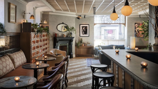 A cozy bar area with wooden tables and benches, a fireplace, and a view of the street. - The Quoin Hotel (Wilmington)