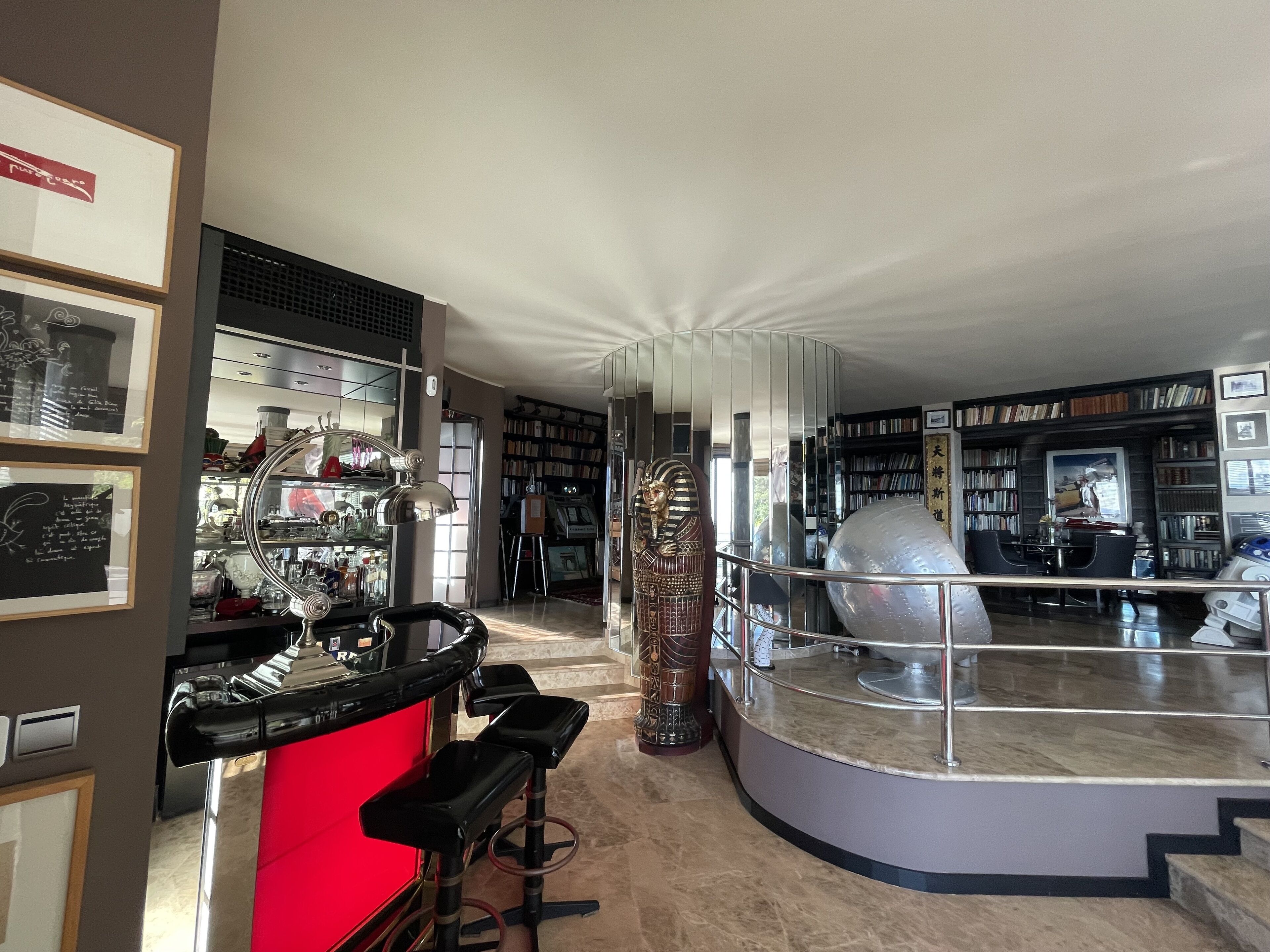 Un interior moderno con una zona de bar, una gran escultura decorativa y una biblioteca repleta de libros.