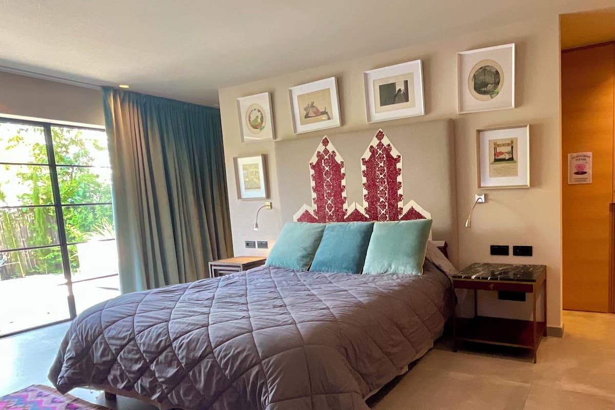 Un dormitorio con una cama grande, una mesita de noche, un aparador y una ventana con cortinas.