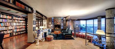 A spacious living room with a large bookshelf, a plush sofa, a coffee table, and a view of the city.