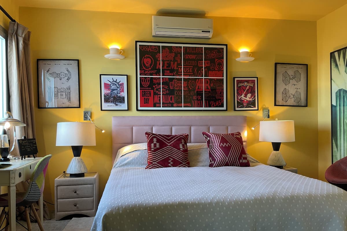 Una habitación de hotel con una cama grande, dos mesitas de noche con lámparas, un escritorio con una silla y varios carteles enmarcados en las paredes.