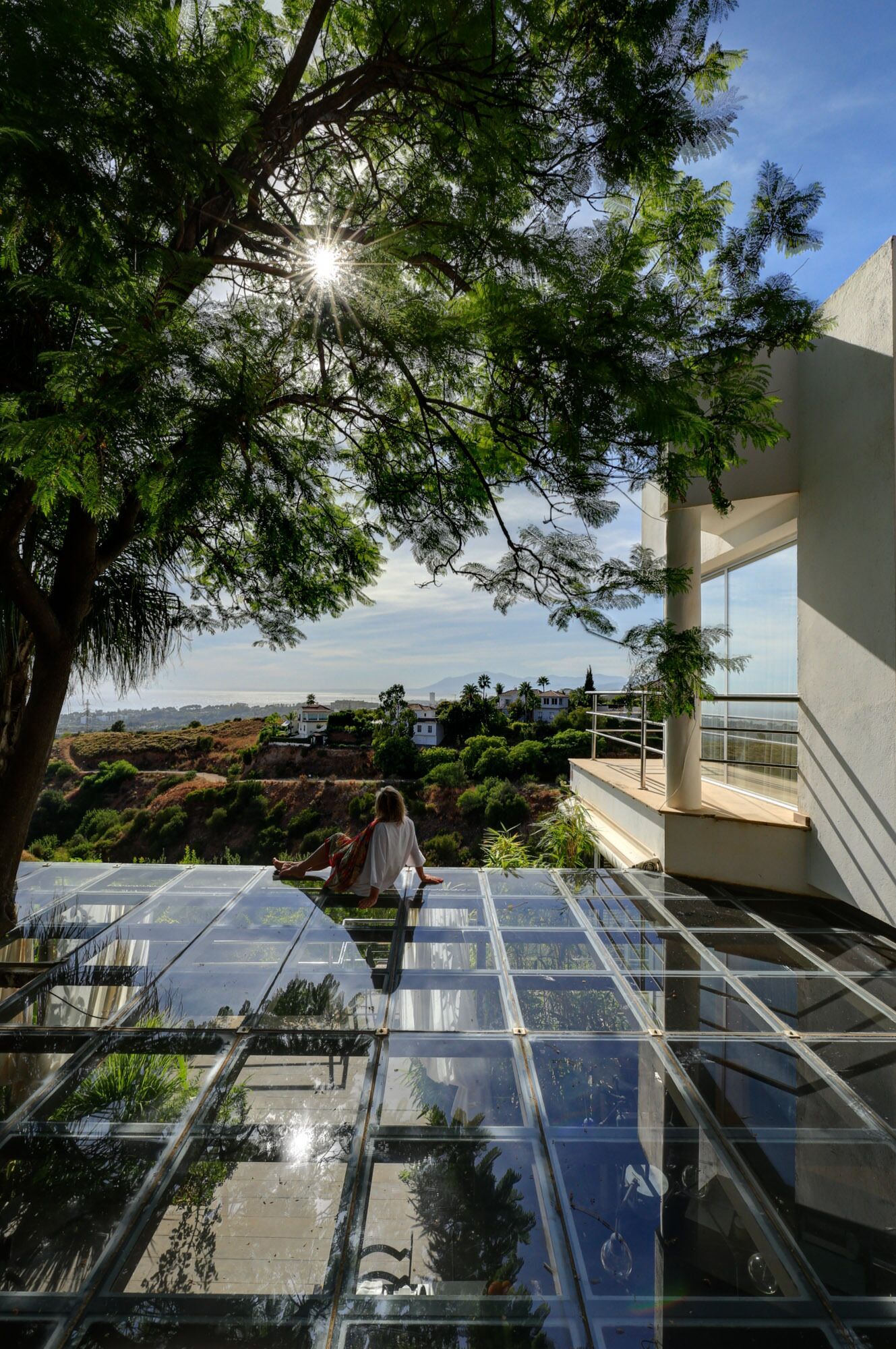 A glass-enclosed terrace with a view of the sea and hills.