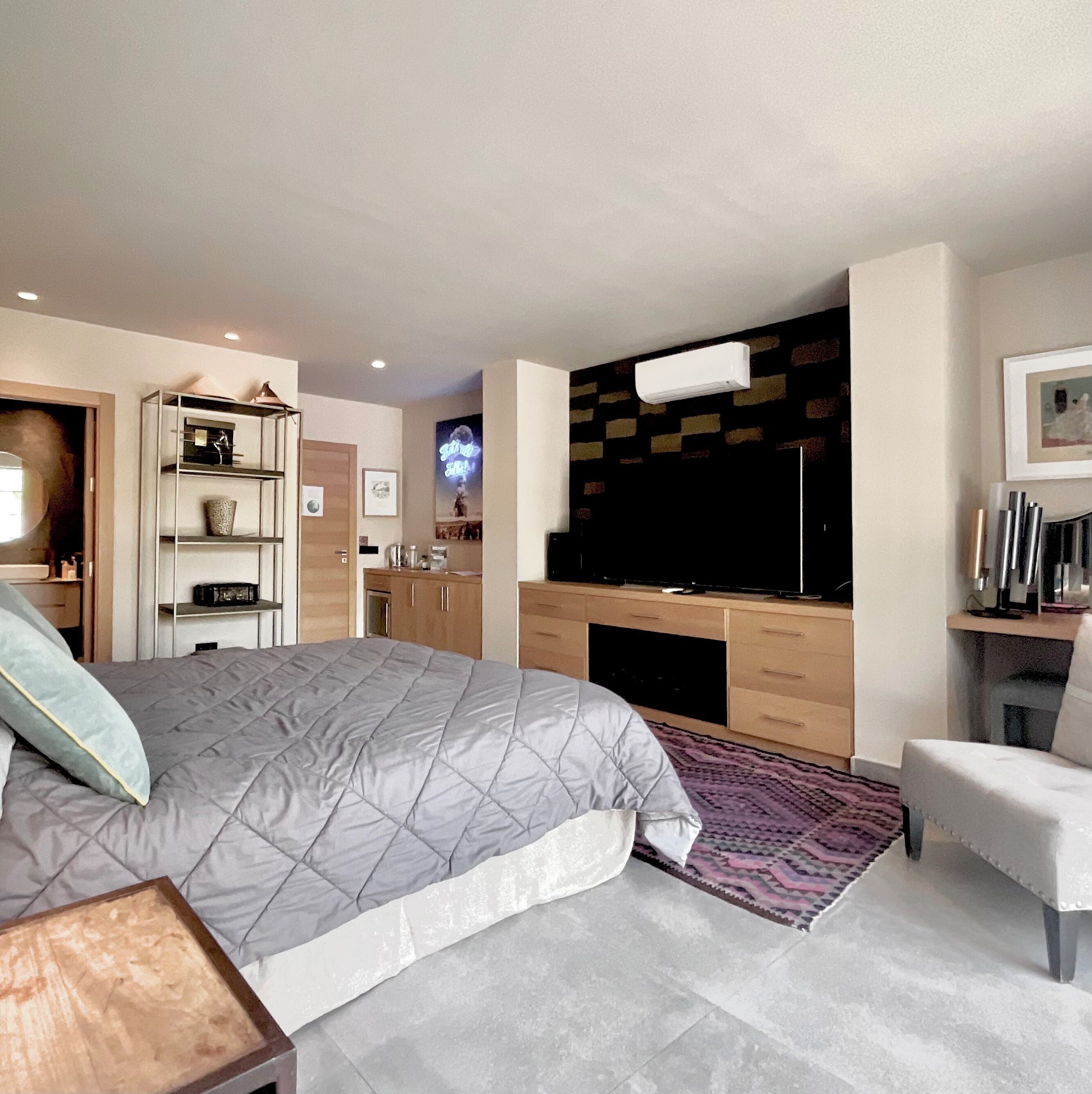 Un dormitorio moderno con una cama grande, un televisor de pantalla plana montado en la pared, un escritorio con una silla y un armario.