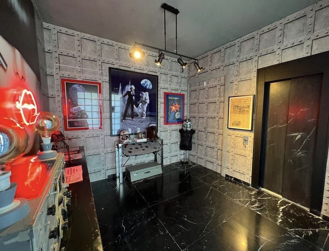 Una habitación con piso de mármol negro, un letrero de neón rojo y un cartel temático del espacio en la pared.