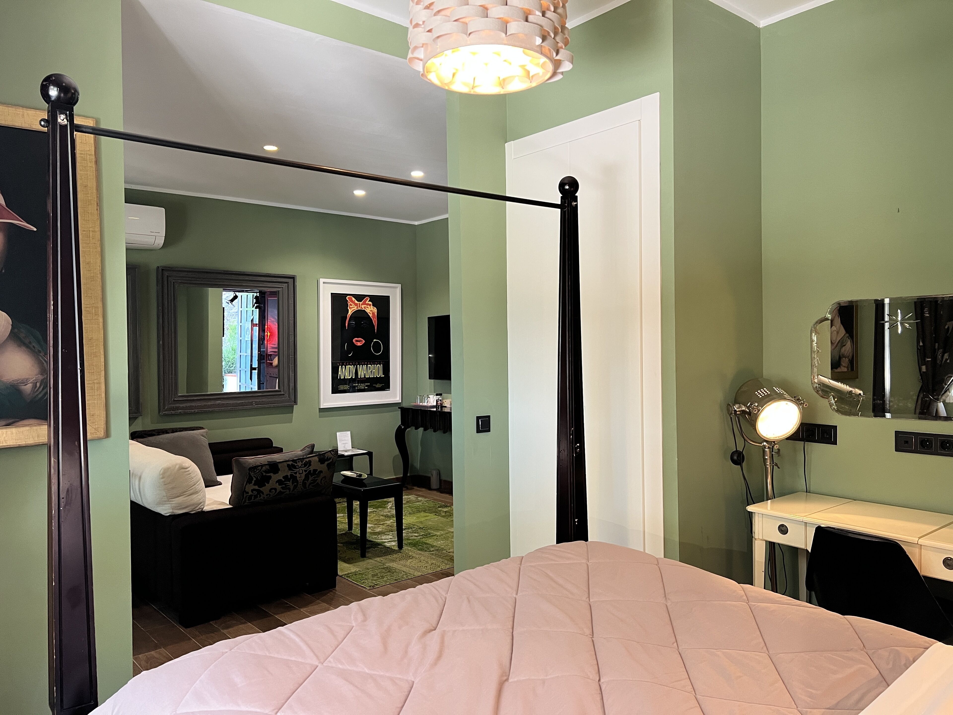 A bedroom with a four-poster bed, a desk with a mirror, and a green wall with artwork.