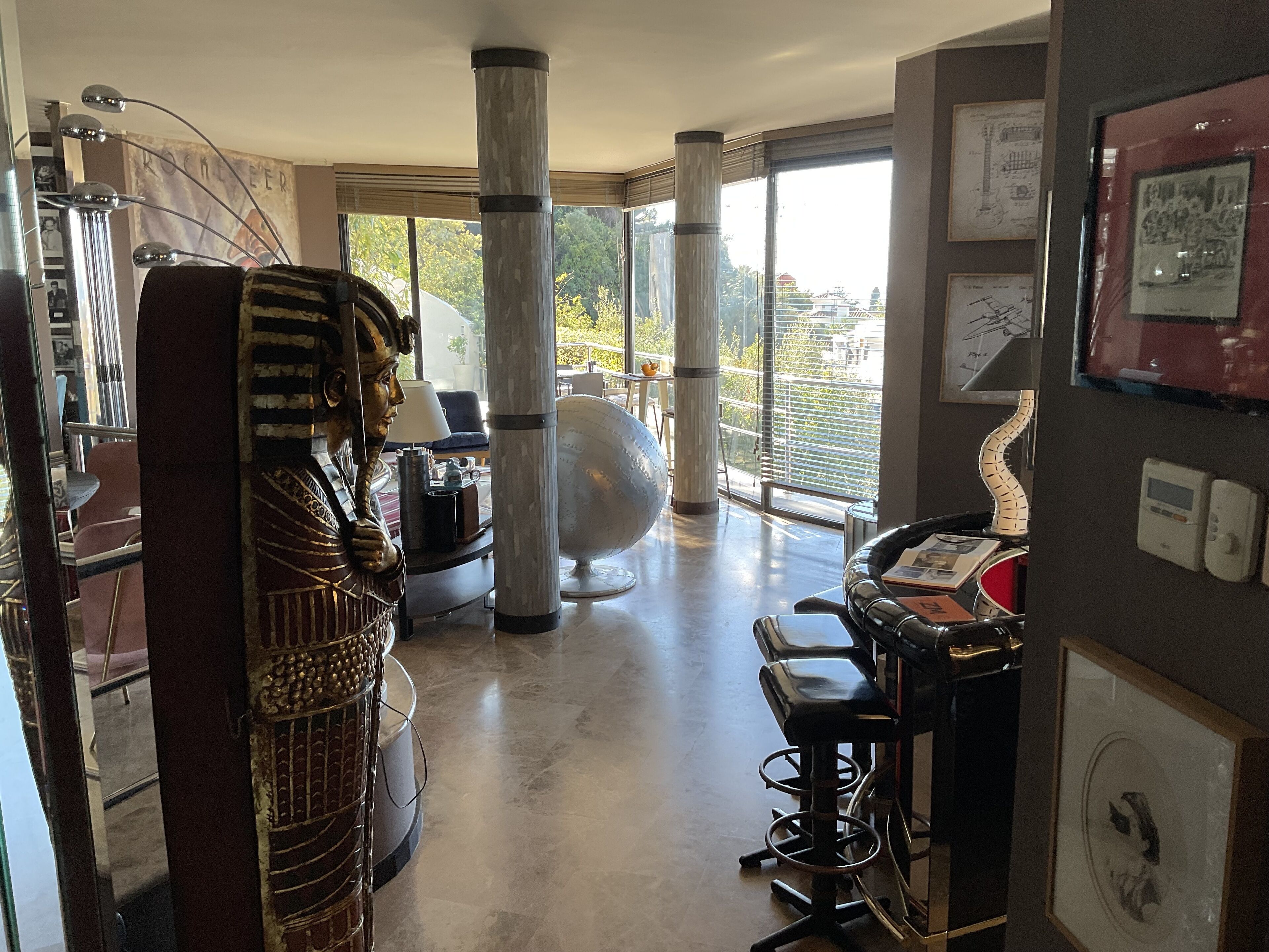 Un interior moderno con una zona de bar, ventanas amplias y esculturas decorativas.