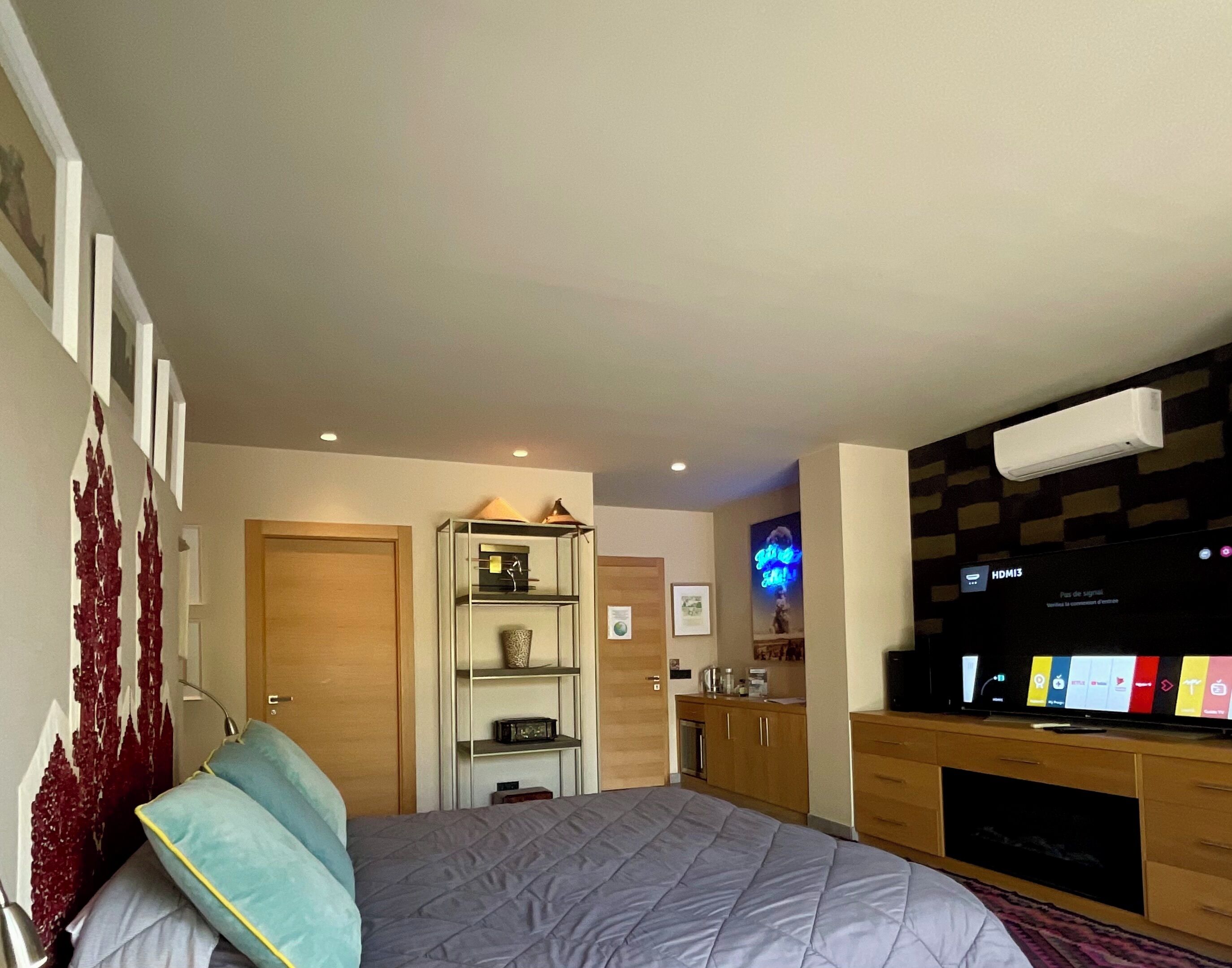 Un dormitorio con una cama, un televisor, una estantería con objetos decorativos y una puerta.