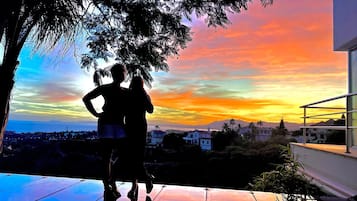 Una pareja está parada en un balcón con vistas a un paisaje urbano al atardecer.