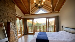 Une chambre spacieuse dotée d’un grand lit, d’un plancher en bois, de murs en pierre et d’un balcon offrant une vue sur la montagne.
