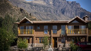 Un bâtiment à deux étages, doté d’une façade en pierre, de balcons en bois et offrant une vue sur un paysage montagneux.