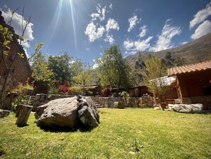A courtyard with a stone wall, a large rock, and a building with a tiled roof.