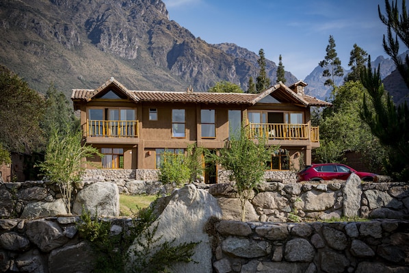 A two-story lodge with a stone facade, large windows, and a balcony overlooking a mountainous landscape.