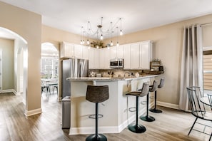Een moderne keuken met witte kasten, een centraal eiland met barkrukken, roestvrijstalen apparatuur en een kroonluchter.