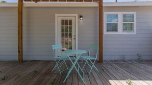 Una veranda riparata con una pergola in legno, una porta bianca e una piccola finestra.