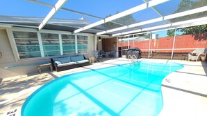 An indoor swimming pool with a glass ceiling, a sofa, and a covered seating area.