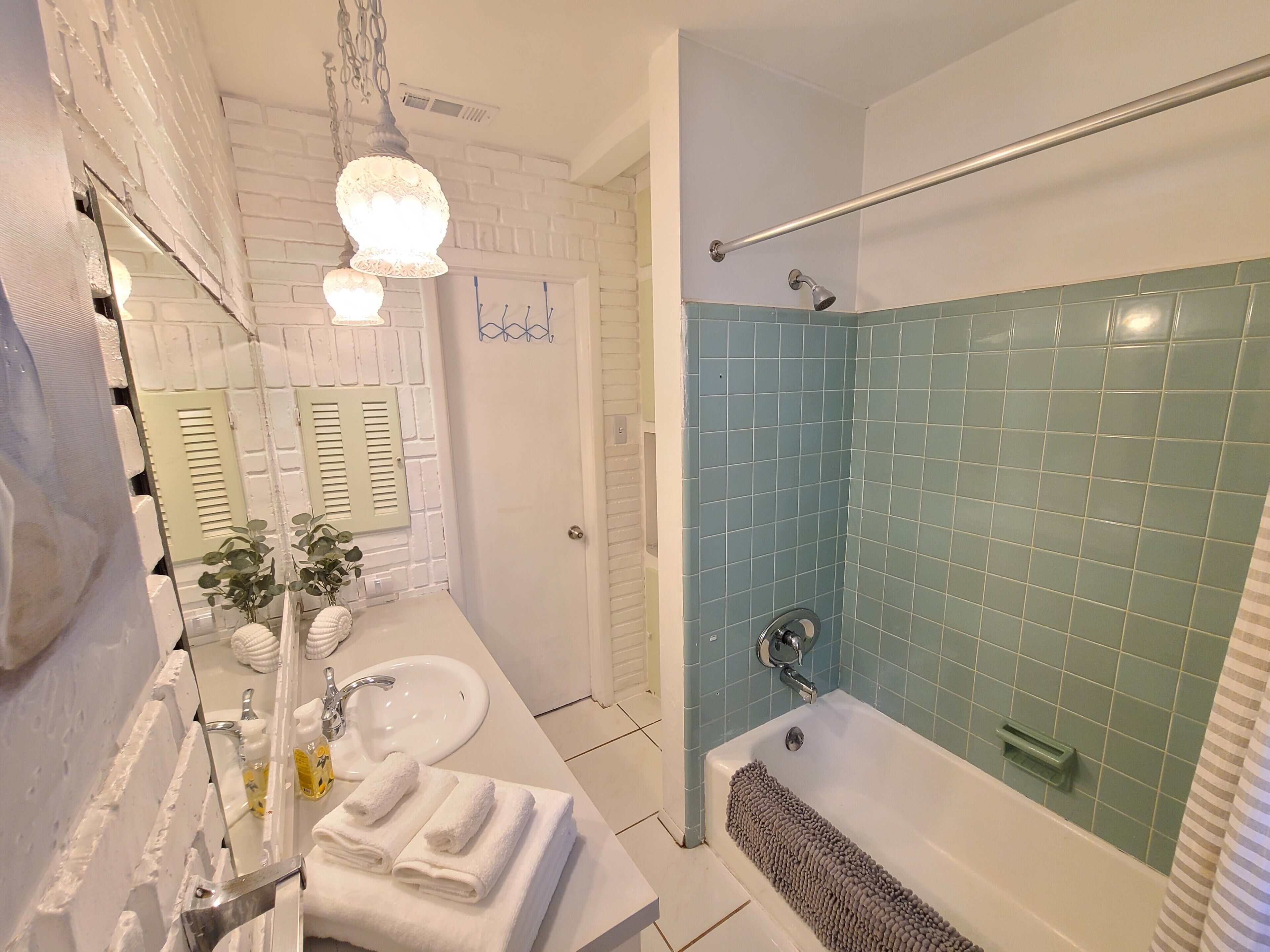 A bathroom with a white sink, a mirror, a towel rack, a shower with blue tiles, and a bathtub.
