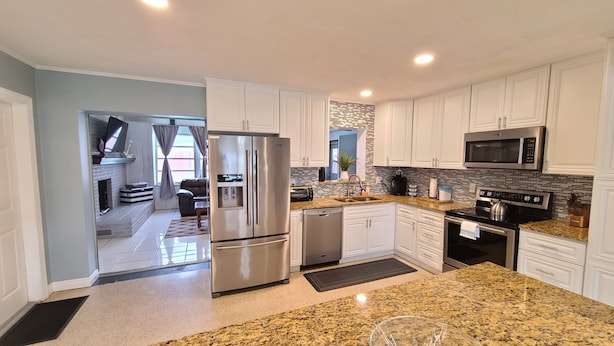 A modern kitchen with white cabinets, stainless steel appliances, granite countertops, and a visible water dispenser.