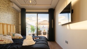 A bedroom with a large bed, a TV mounted on the wall, and a view of the outdoors. - Vintage Dead Sea with Pool & Rooftop (Casablanca)