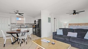 Eine moderne Küche mit weißen Schränken, einem Esstisch mit Stühlen, einem Kühlschrank und einem Deckenventilator.