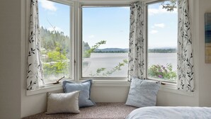 Una habitación con ventanal panorámico con vistas al agua, una cama y un asiento junto a la ventana con cojines.