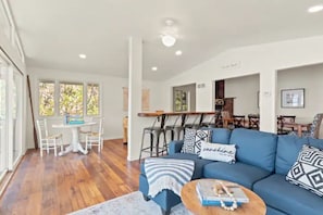 Un salon moderne avec un canapé bleu, une table basse en bois et un coin repas comprenant une table et des chaises blanches.