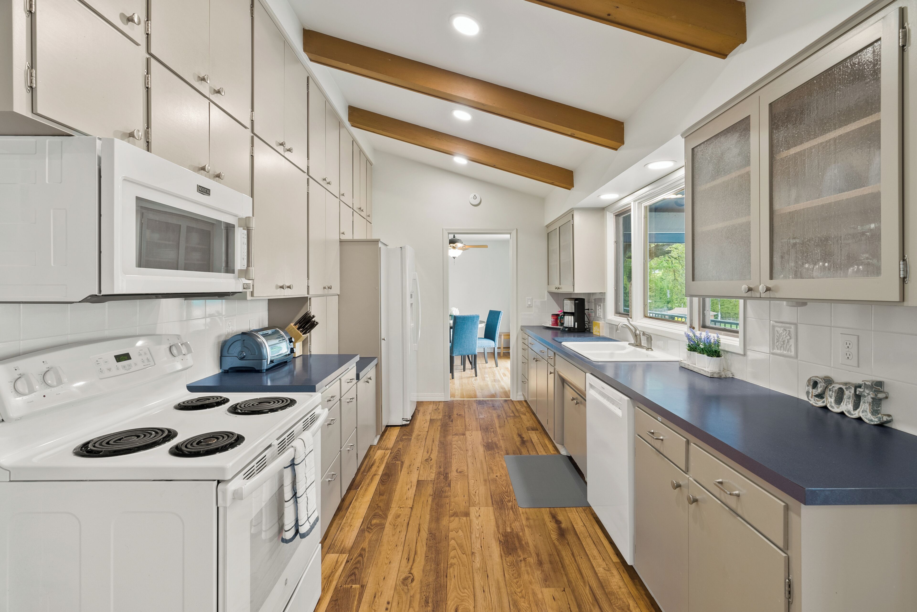 A modern kitchen with white cabinets, a stove, microwave, and a blue toaster.