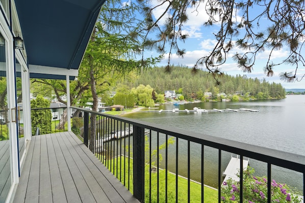 Une terrasse en bois avec une balustrade donnant sur un lac, entourée d’arbres et de maisons.